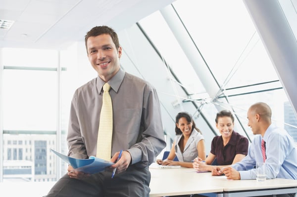 Smiling male worker with yellow i-style tie sitting on table in meeting