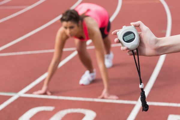 Close-up of a hand timing a blurred young woman's run on the running track