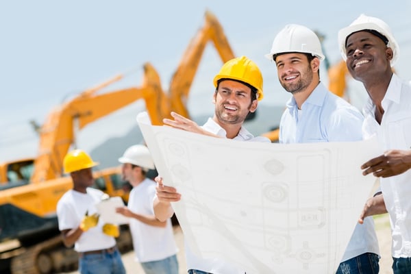 Group of workers at a construction site holding blueprints