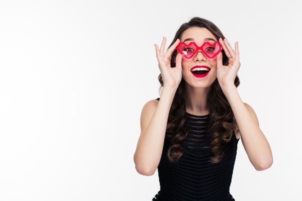 Portrait of happy funny curly young woman with retro hairstyle in red heart shaped glasses