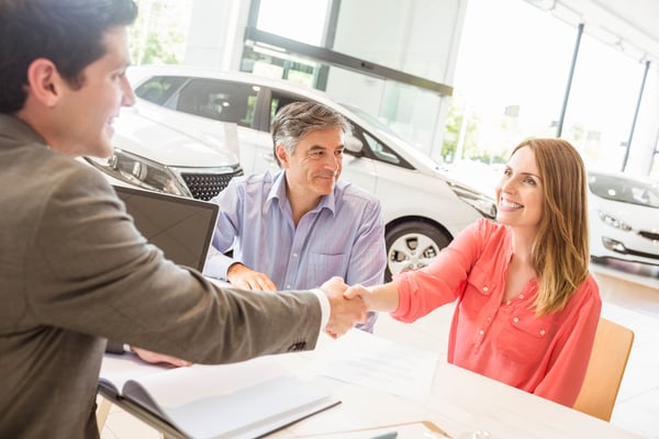 couple shaking hands with salesperson at car dealership