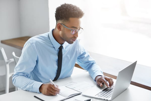 bigstock-Handsome-Young-Dark-skinned-Man in c-style blue on computer with pen and notebook